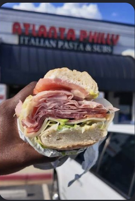 Close-up of a loaded Italian sub held up outside the storefront