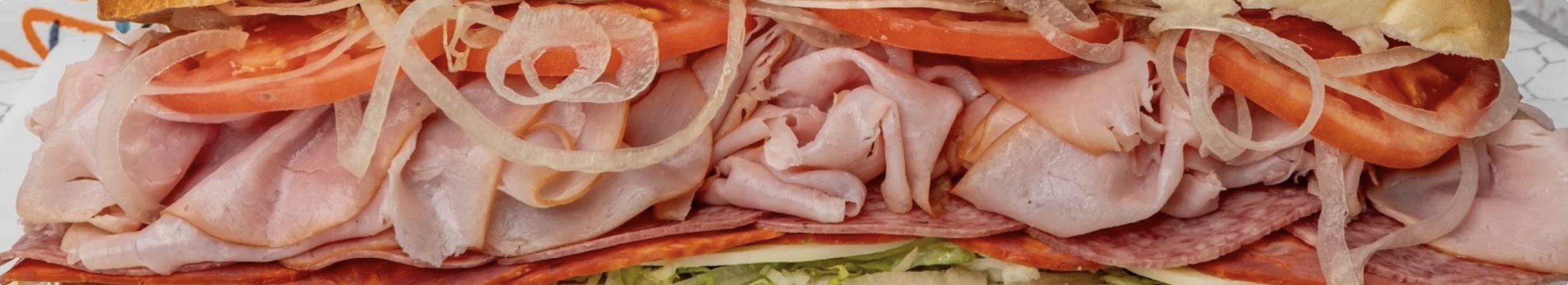 Close-up of a loaded Italian sub with ham, salami, onions and tomato