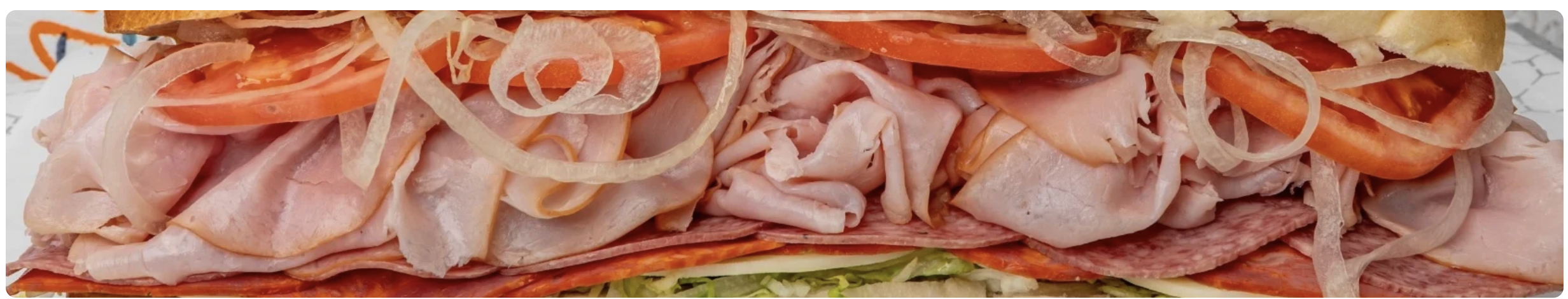 Close-up of a loaded Italian sub with ham, salami, onions and tomato